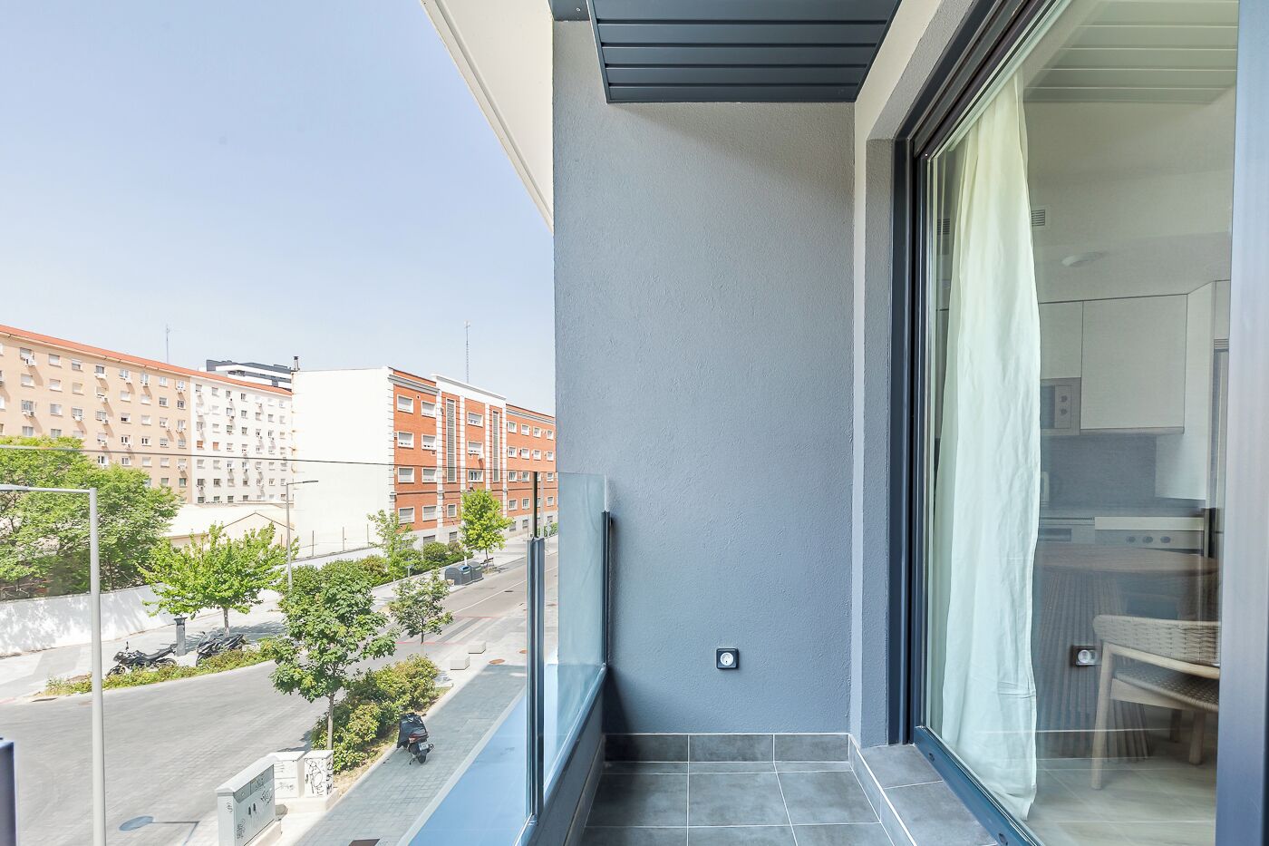 Un balcón con vista a la ciudad, una pequeña zona de estar al aire libre y una ventana con cortina.