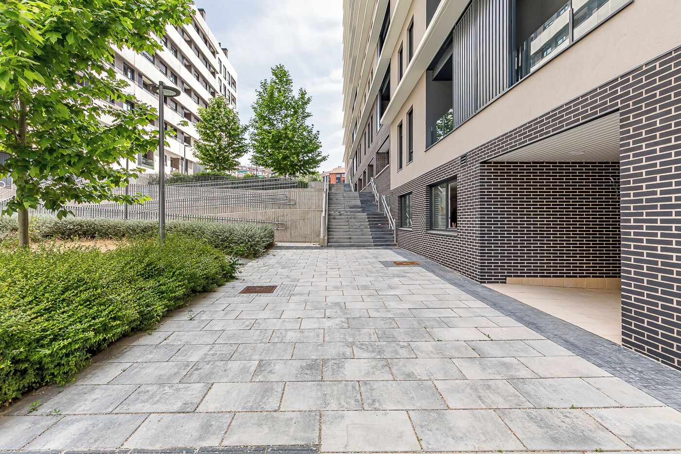 Ein moderner Stadtweg mit einer Ziegelwand an einer Seite und einem Gebäude mit großen Fenstern an der anderen.
