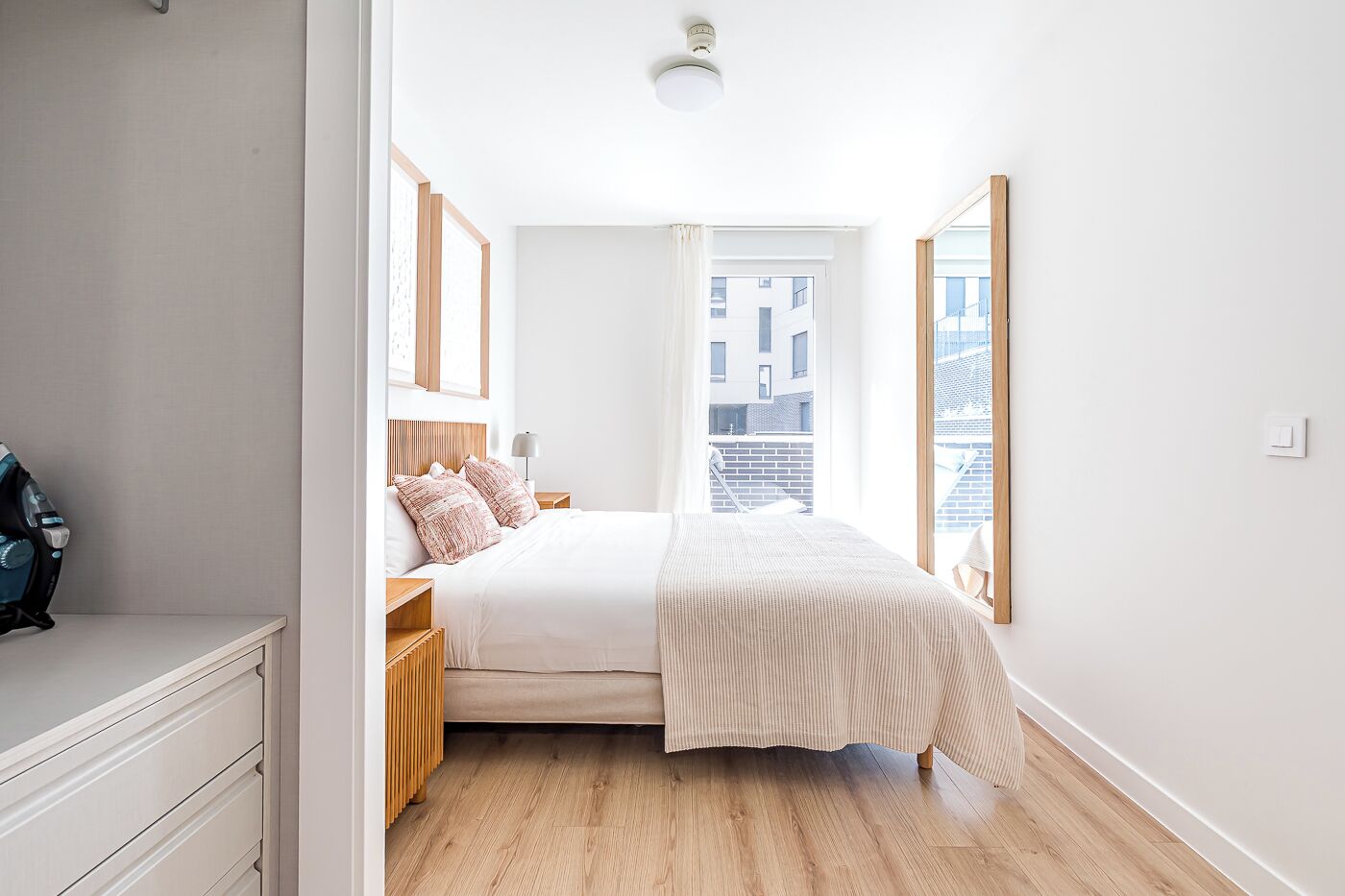 A modern bedroom with a large bed, wooden headboard, and a view of the city through a window.