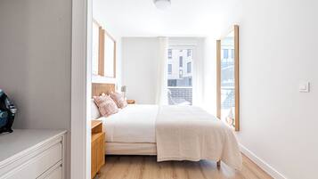 A modern bedroom with a large bed, wooden headboard, and a view of the city through a window.