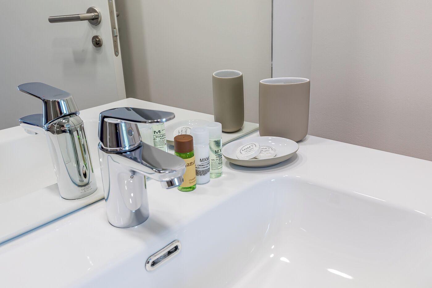 A modern bathroom with a chrome faucet, a mirror, and toiletries on the sink.