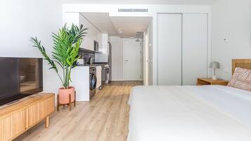 Habitación de hotel moderna con una cama grande, televisor, espacio para cocinar y una planta en maceta.