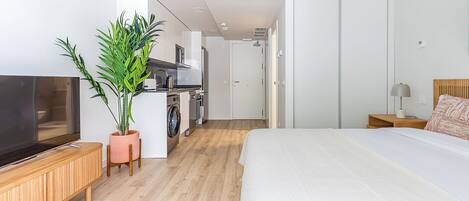 Habitación de hotel moderna con una cama grande, televisor, espacio para cocinar y una planta en maceta.