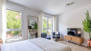 Una habitación de hotel moderna con una cama grande, un televisor, una mesita pequeña y una zona de estar con sillas.