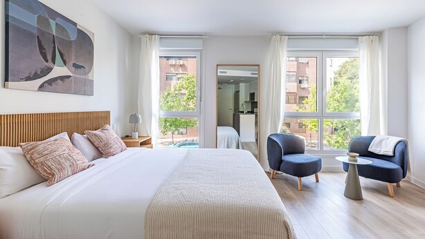 Un hotel moderno con una cama grande, dos sillones, una mesita y un cuadro en la pared.