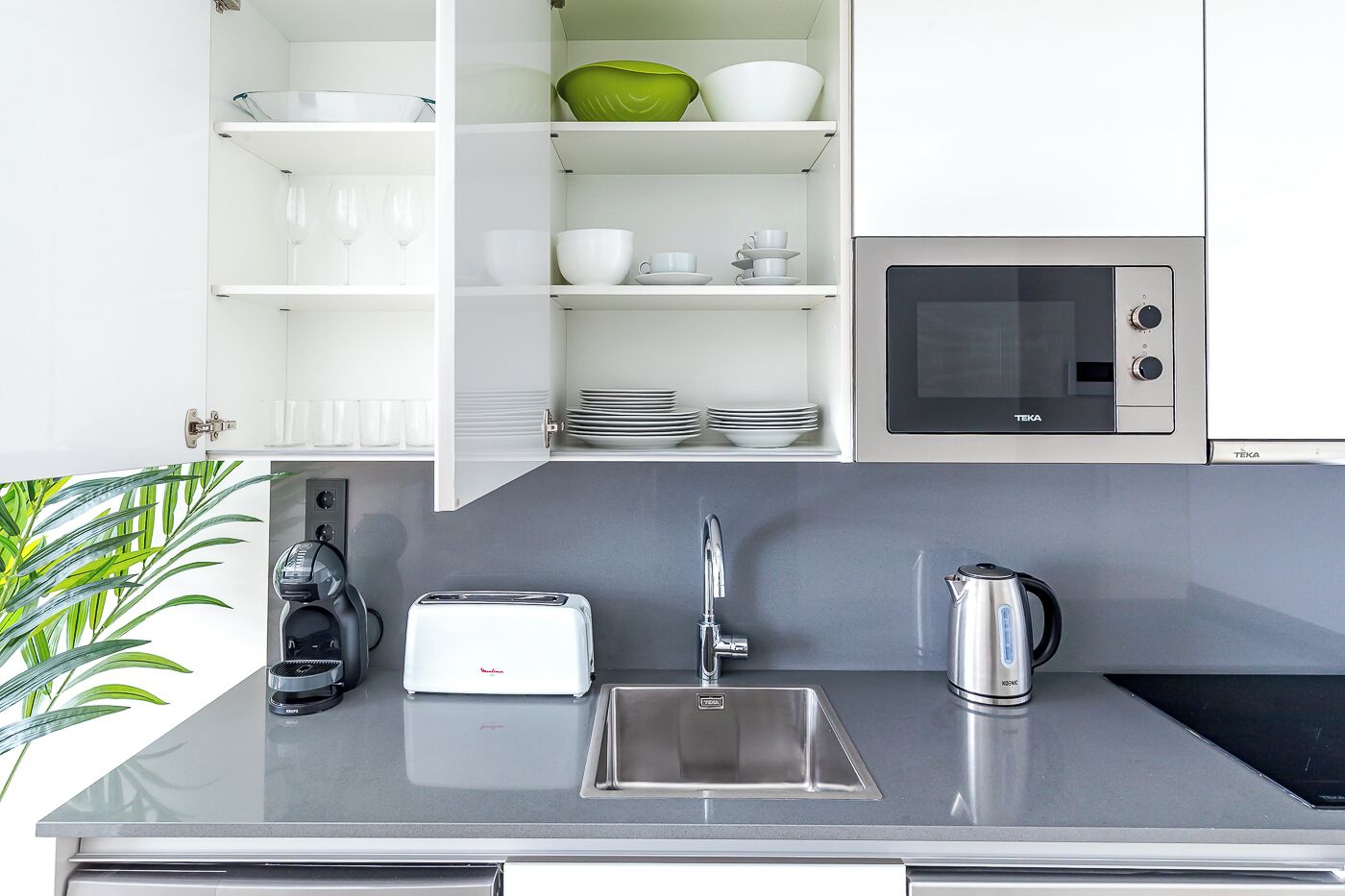 A modern kitchen with a built-in microwave, a toaster, a sink, and a kettle.