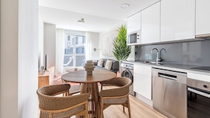 Una cocina moderna con electrodomésticos de acero inoxidable, un comedor con sillas de mimbre y un amplio ventanal con vistas a la ciudad.