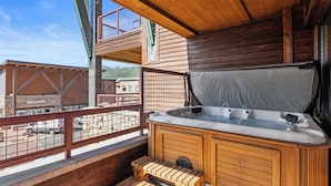 A wooden deck with a hot tub, wooden benches, and a view of a mountain and a building labeled "Bartolo's".