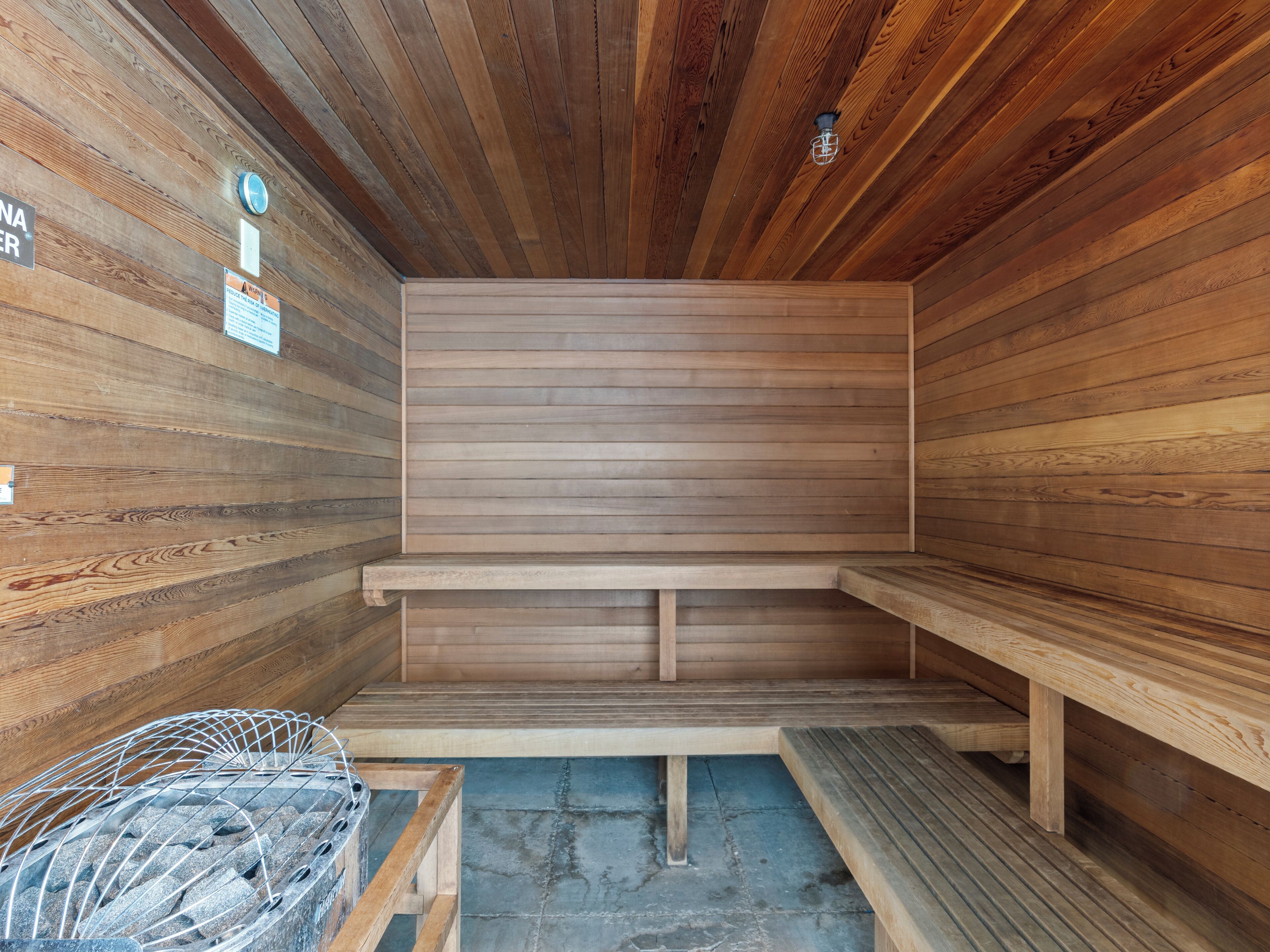 Una sauna con paredes y bancos de madera, un banco de metal y un suelo de piedra.