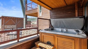 A wooden deck with a hot tub, wooden benches, and a view of a mountain.