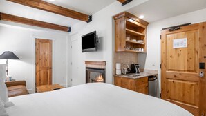 Une chambre avec un grand lit, un téléviseur fixé au mur, une cheminée, des meubles en bois et une porte avec une pancarte.