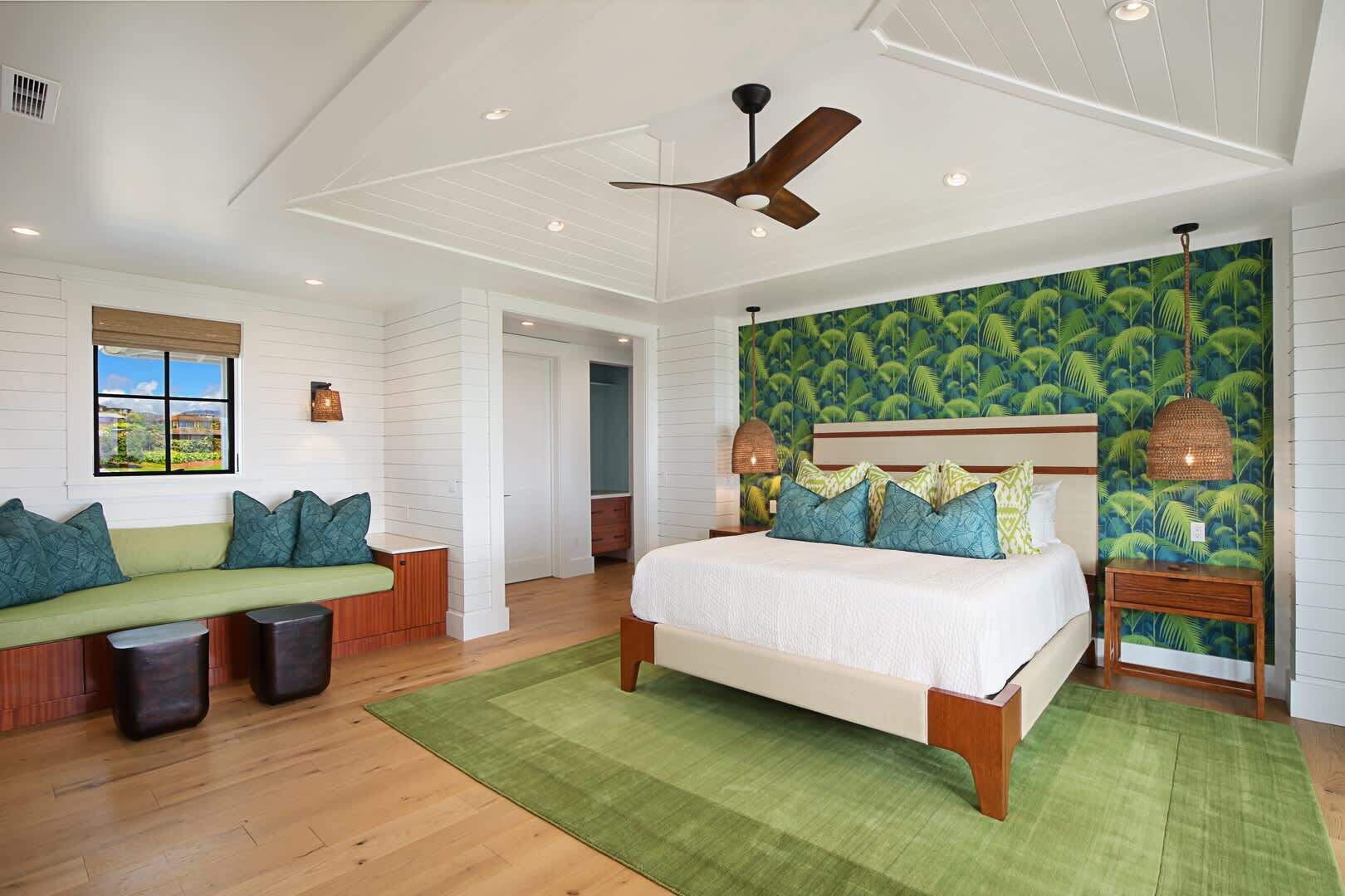 Un dormitorio con una cama grande, un banco con cojines, un ventilador de techo y un papel tapiz tropical.