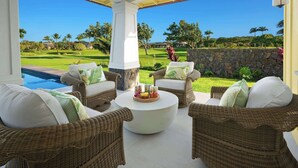 Un espacio exterior techado con mobiliario de mimbre y una mesa de centro, con vistas a un césped cuidado y un campo de golf.