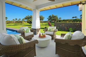 Un espacio exterior techado con mobiliario de mimbre y una mesa de centro, con vistas a un césped cuidado y un campo de golf.