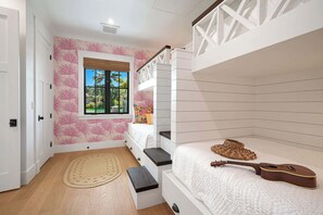 Un dormitorio con una cama litera, una ventana con vistas a palmeras, una guitarra y una alfombra tejida.