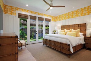 Ein Schlafzimmer mit einem großen Bett, einem Deckenventilator und Gartenblick durch Glastüren.