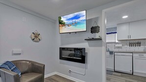 Una sala de estar moderna con un televisor montado, un sofá de cuero acogedor, una chimenea y una cocina con armarios blancos y lavavajillas.