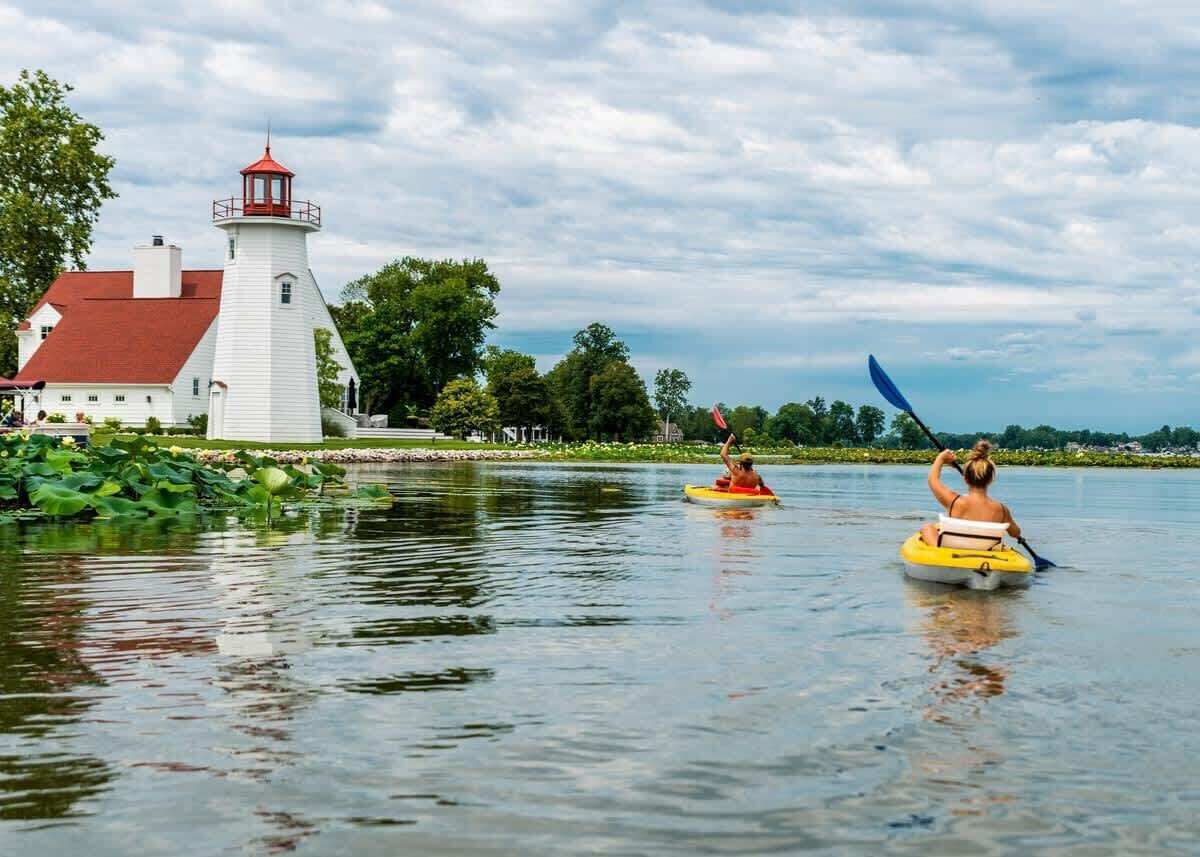 A lighthouse and a building with a red roof by a calm lake.