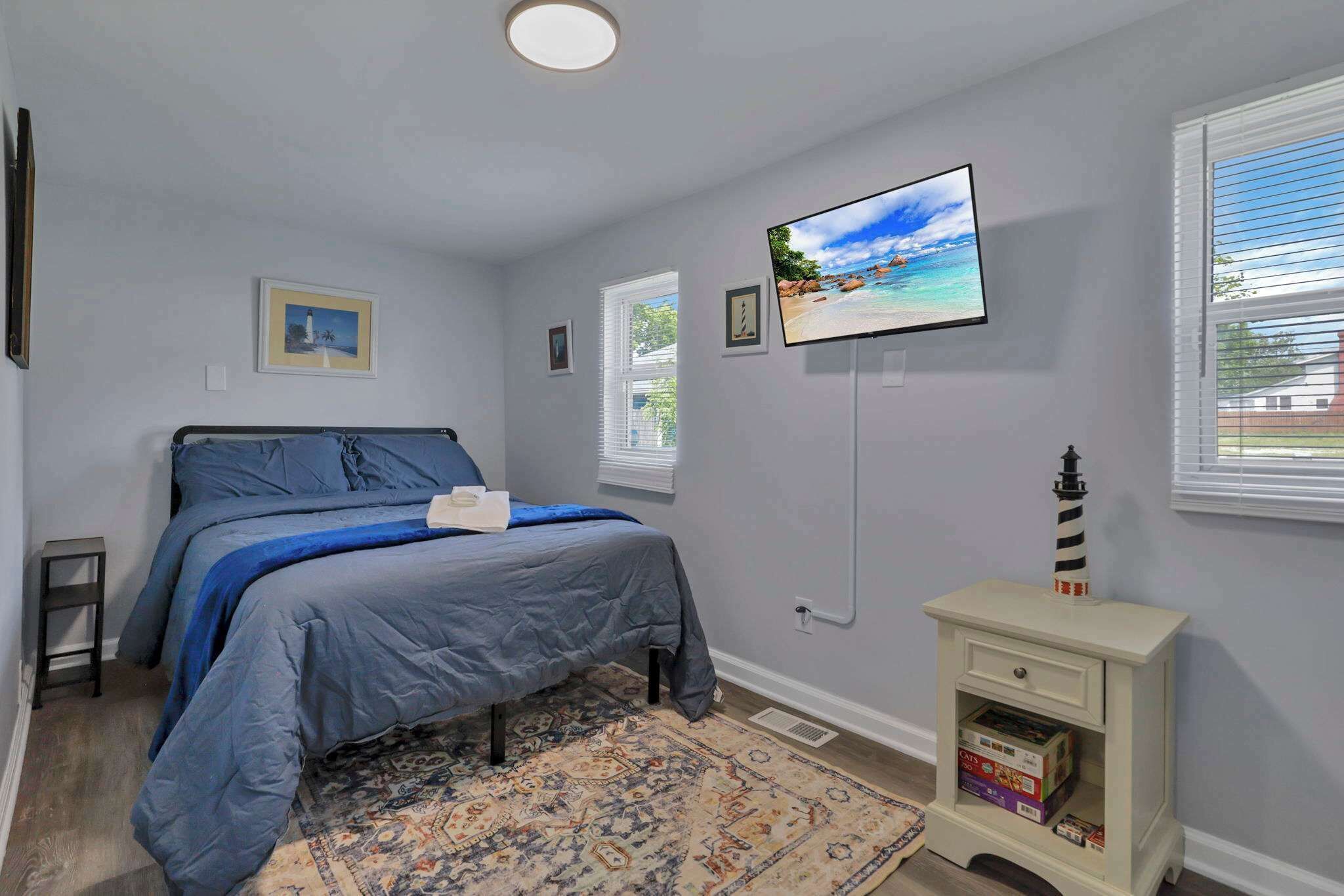 Une chambre à coucher avec un lit, un téléviseur fixé au mur, une petite table de chevet et une fenêtre avec des stores.