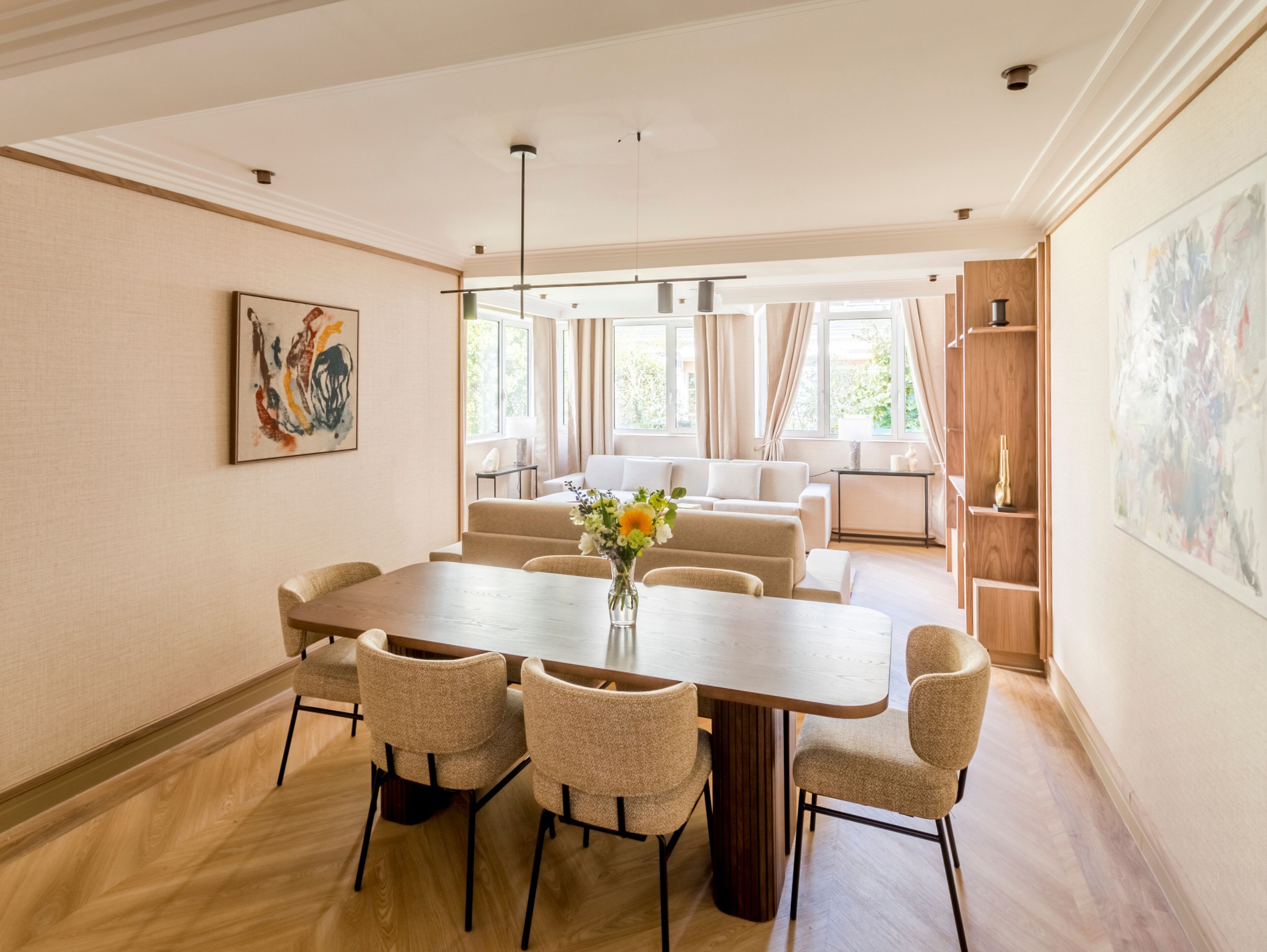 A dining area with a wooden table and four chairs, a vase with flowers, and a painting on the wall.