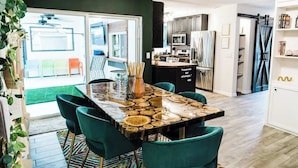 A modern kitchen with a central island, dark green chairs, and a view to a balcony.