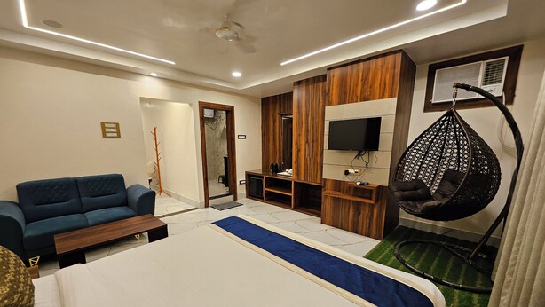 A modern hotel room with a bed, a sofa, a hanging chair, a TV, and a wardrobe. - HOTEL MAA LAXMI PALACE (Deoghar)