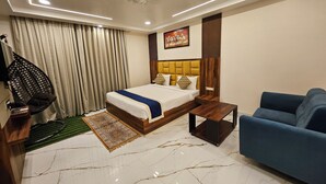 A modern hotel room with a large bed, a blue sofa, a wooden nightstand, and a ceiling fan. - HOTEL MAA LAXMI PALACE (Deoghar)