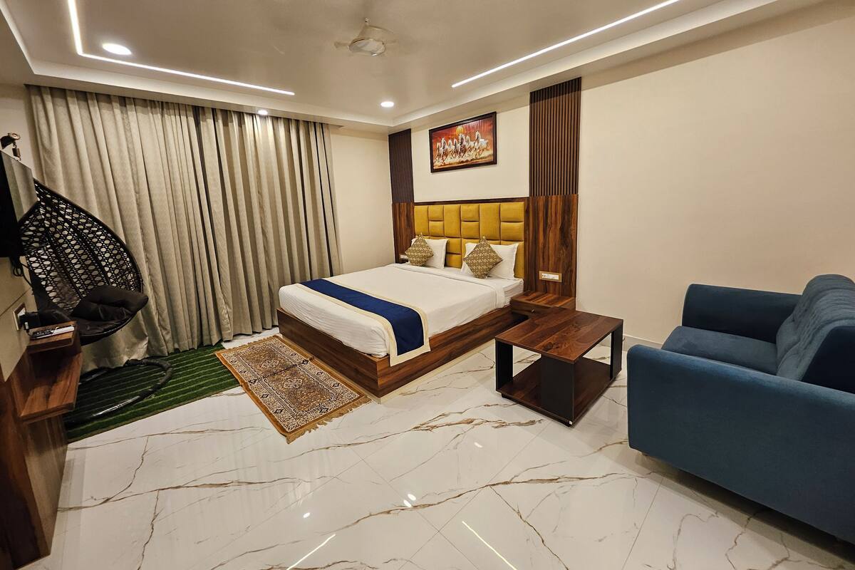 Quarto de hotel moderno com uma cama grande, um sofá azul, uma mesa de cabeceira de madeira e um ventilador de teto.