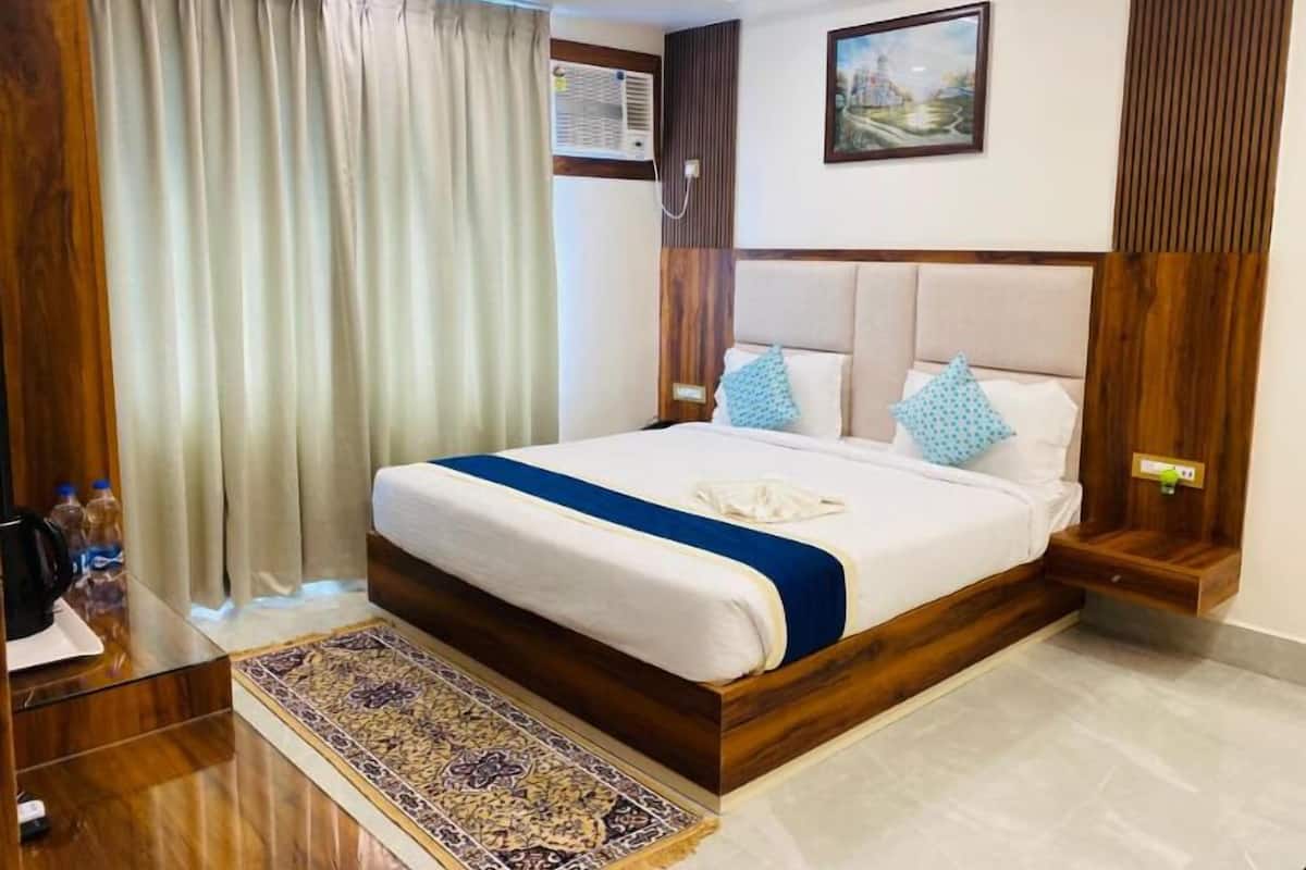 Quarto de hotel com uma cama grande, cabeceira de madeira, um quadro na parede e uma janela com cortinas.