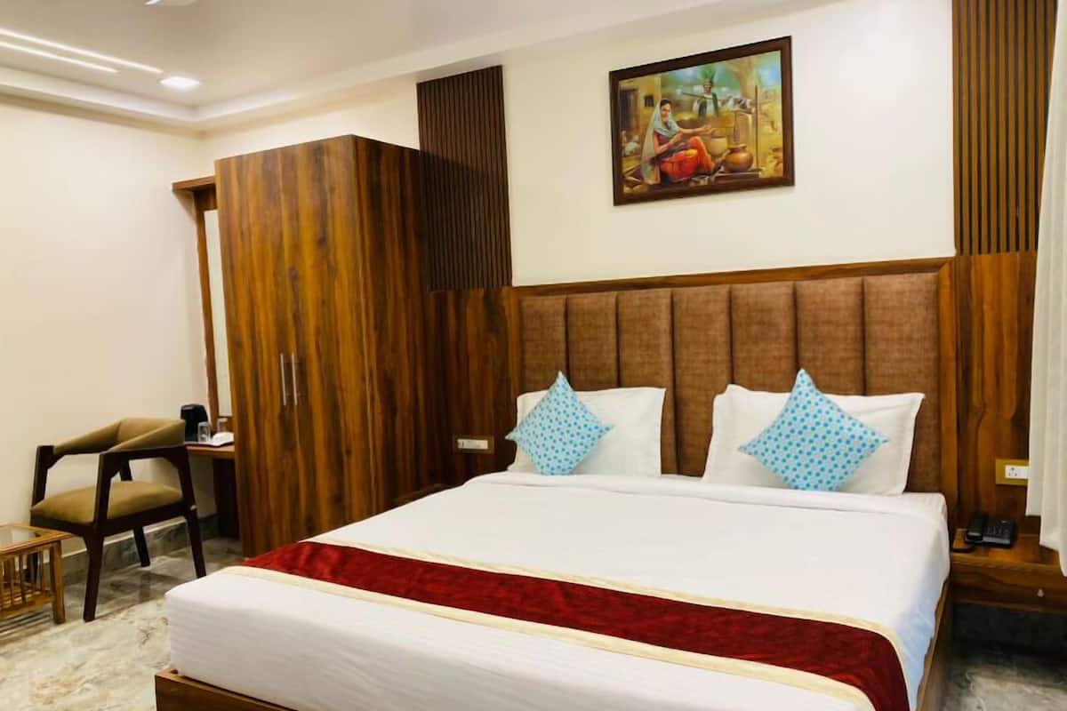 Quarto de hotel com uma cama grande, cabeceira de madeira, um quadro na parede, uma cadeira e uma mesa pequena.