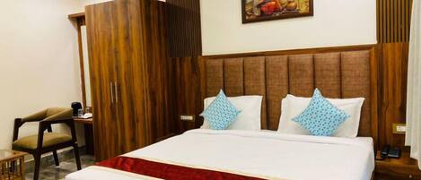 A hotel room with a large bed, wooden headboard, a painting on the wall, a chair, and a small table.
