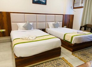 A hotel room with two beds, each with a wooden headboard, white bedding, and a green accent. There is a patterned rug on the floor and a painting on the wall. - HOTEL MAA LAXMI PALACE (Deoghar)