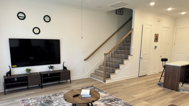 Ein modernes Wohnzimmer mit Flachbildfernseher, dunklen Holzmöbeln, einer Treppe und einem runden Couchtisch.