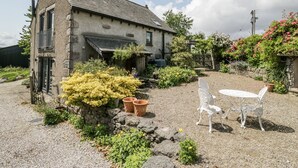 A stone house with a gravel patio, a small garden, and a white metal table and chairs. - Threagill (Carnforth)