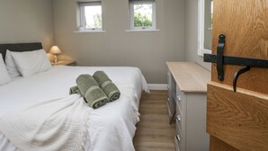 A bedroom with a bed, two windows, a nightstand, a lamp, and a wooden dresser. - Threagill (Carnforth)