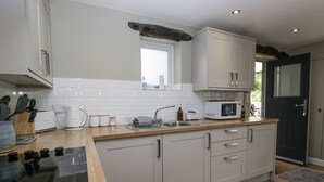 A modern kitchen with white cabinets, a wooden countertop, a built-in microwave, and a window above the sink. - Threagill (Carnforth)