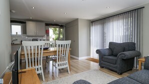 A modern living room with a grey sofa, a dining table with white chairs, and a kitchen in the background. - Threagill (Carnforth)