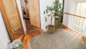 A hallway with wooden doors, a potted plant, a woven rug, and a window with a white railing. - 18 Main Street (Fishguard)