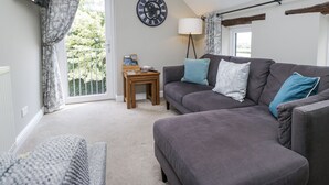 A living room with a grey sofa, a small wooden table, a floor lamp, and a large wall clock.
