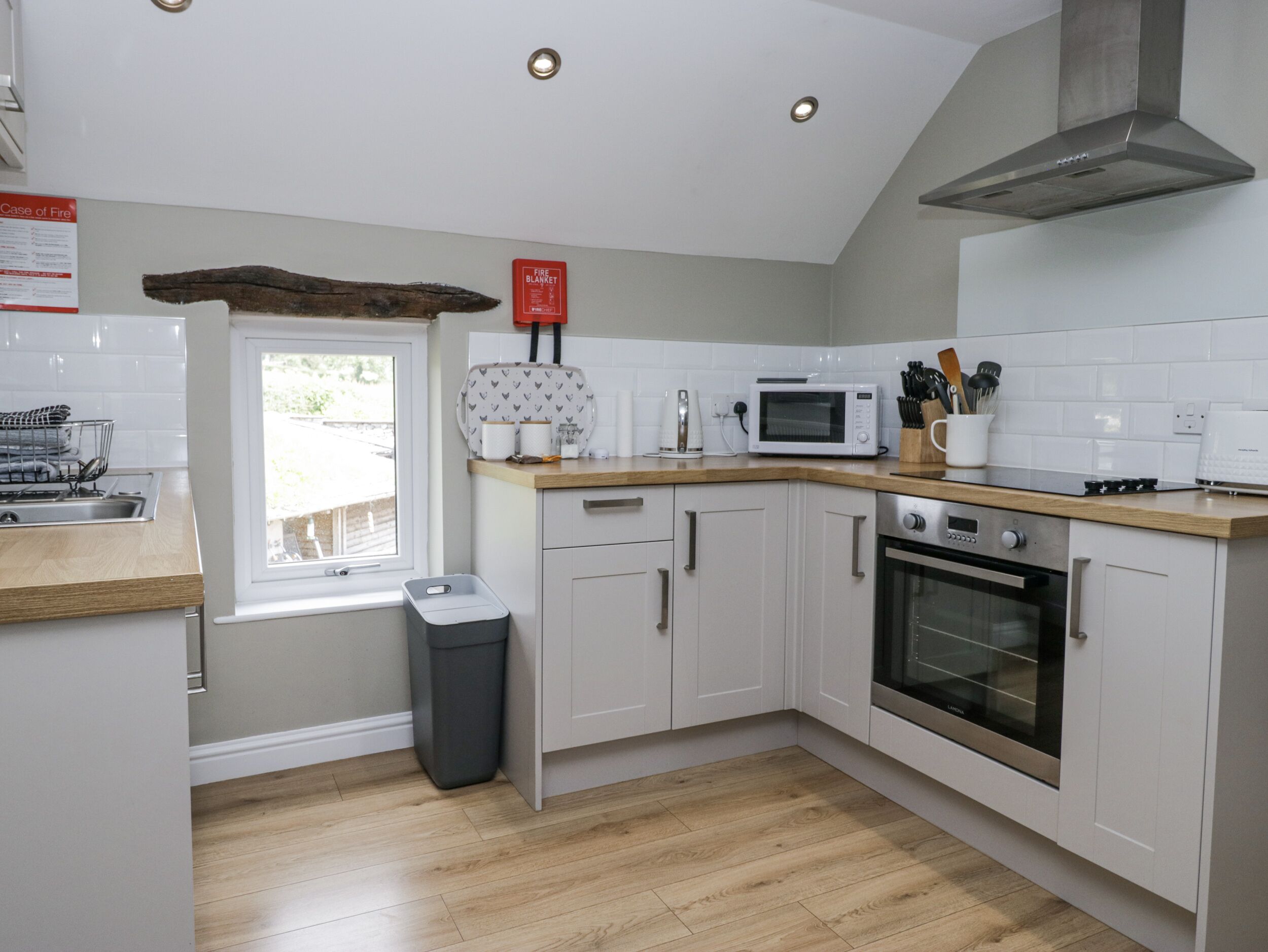 A modern kitchen with white cabinets, a stainless steel range hood, a microwave, and a window with a view.
