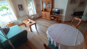 A cozy living room with a sofa, a dining table, a television, and a cabinet. - Apartment 'Haarkotten' with Private Terrace, Shared Garden and Wi-Fi (Steinfurt)