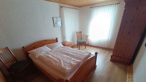 A wooden bed in a room with a chair, a nightstand, and a window with curtains. - Apartment 'Haarkotten' with Private Terrace, Shared Garden and Wi-Fi (Steinfurt)