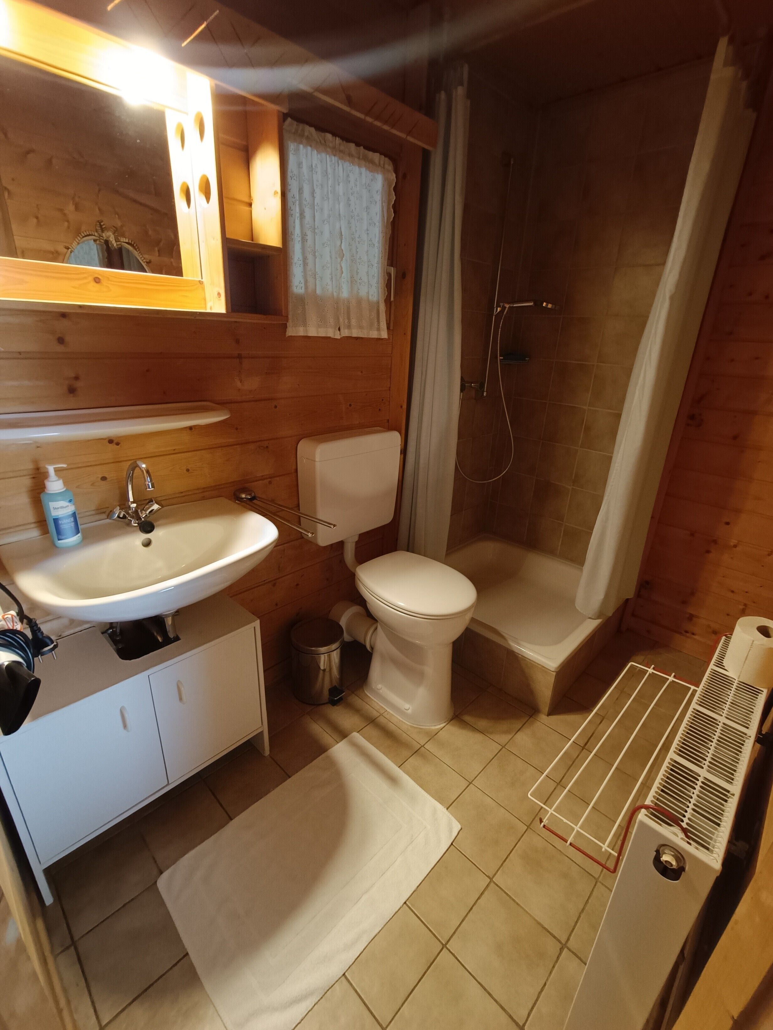A bathroom with a sink, toilet, shower, and a radiator.