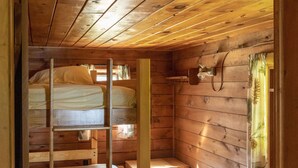 L’intérieur d’une cabane en bois, avec des lits superposés, une échelle en bois et une petite étagère en bois.