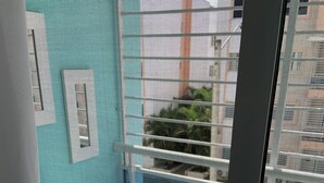 Une pièce avec un banc blanc, une petite table sur laquelle est posée une plante en pot, et une vue à travers une fenêtre grillagée.