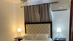 Une chambre à coucher comprenant un lit, deux tables de chevet avec des lampes, un ventilateur de plafond et un appareil de climatisation.