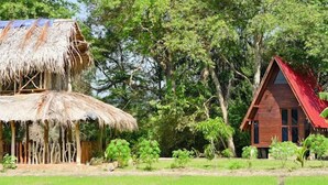 A traditional thatched-roof structure and a modern wooden building with a red roof, surrounded by lush greenery. - VR Nature Cottage (Wellawaya)