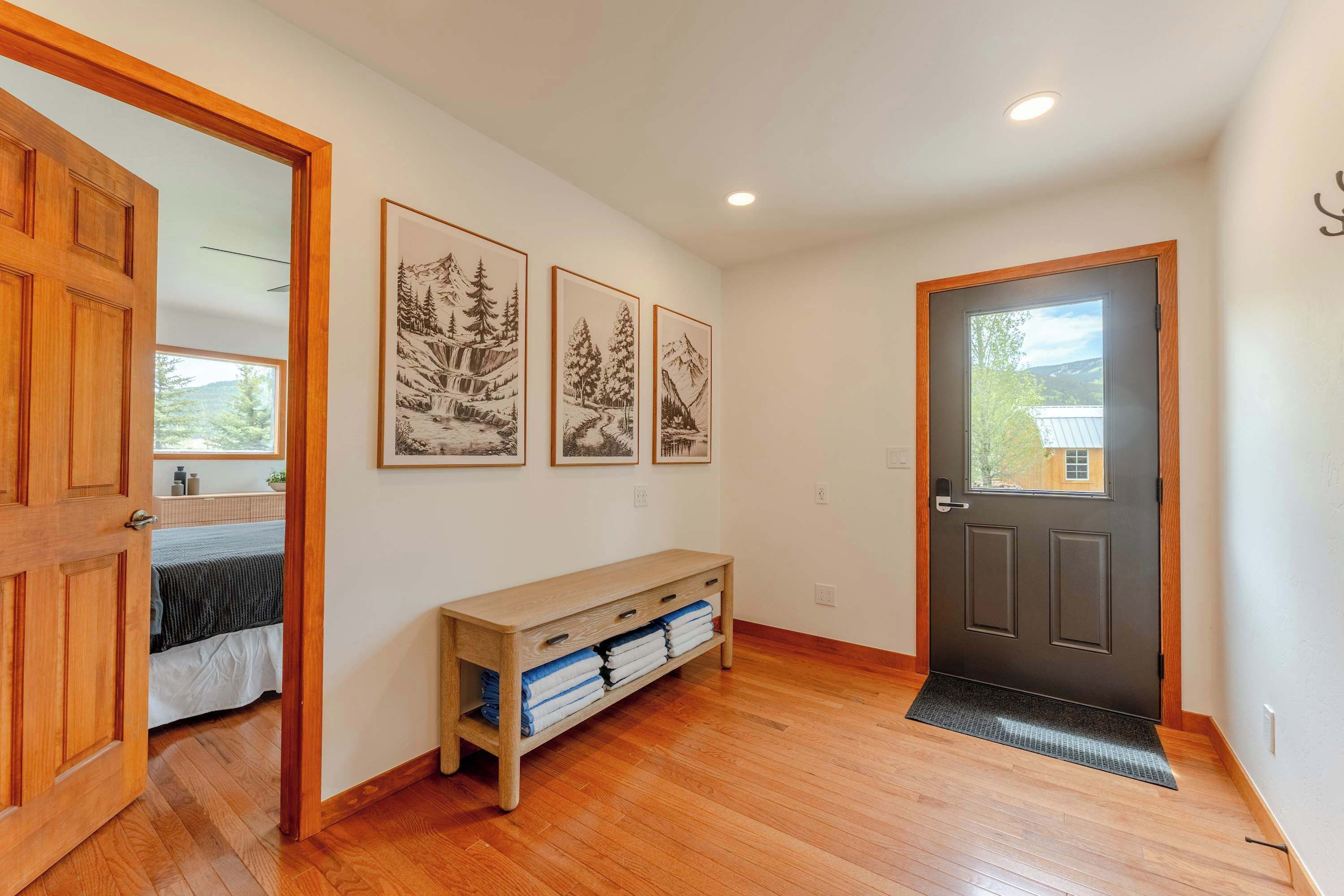 A hallway with wooden flooring, a bench with towels, and framed pictures on the wall.