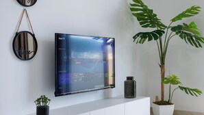 A modern living room with a flat-screen TV, a white entertainment unit, a potted plant, and wall-mounted decor. - Captain's Residence (Ksamil)