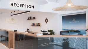 A reception area with a wooden reception desk, a large hanging light fixture, and a wall-mounted sign that reads "RECEPTION". - Captain's Residence (Ksamil)